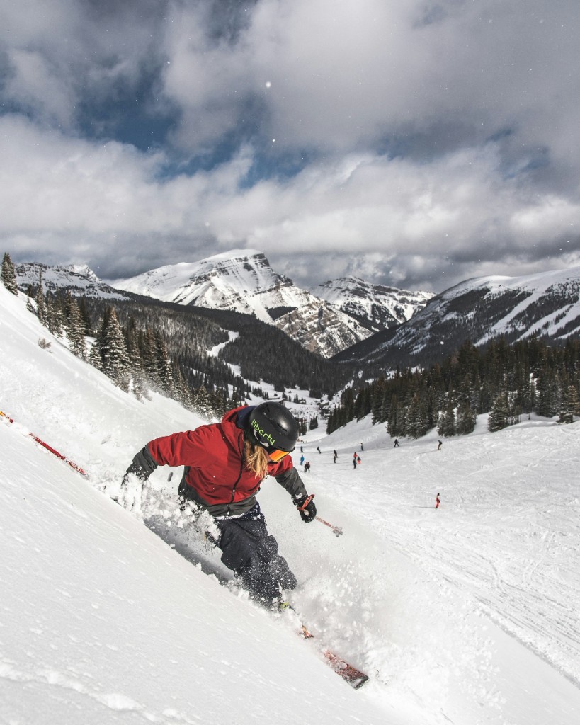 Skier turning on a steep snowy slope with mountain peaks in the distance